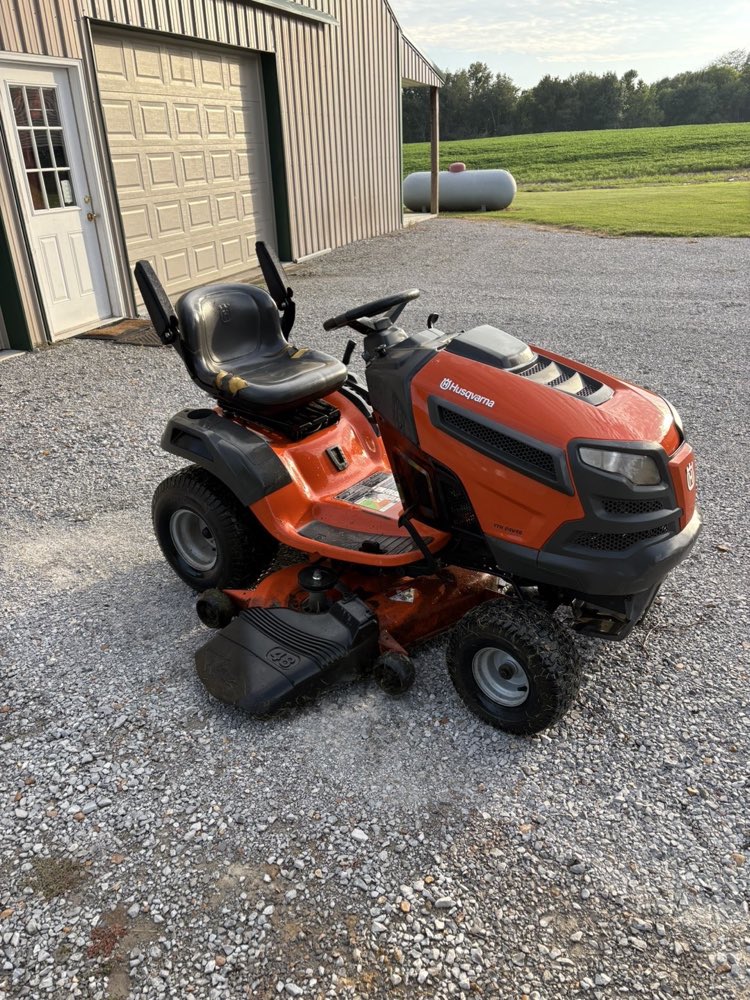 An orange Husqvarna riding mower parked outside a shop