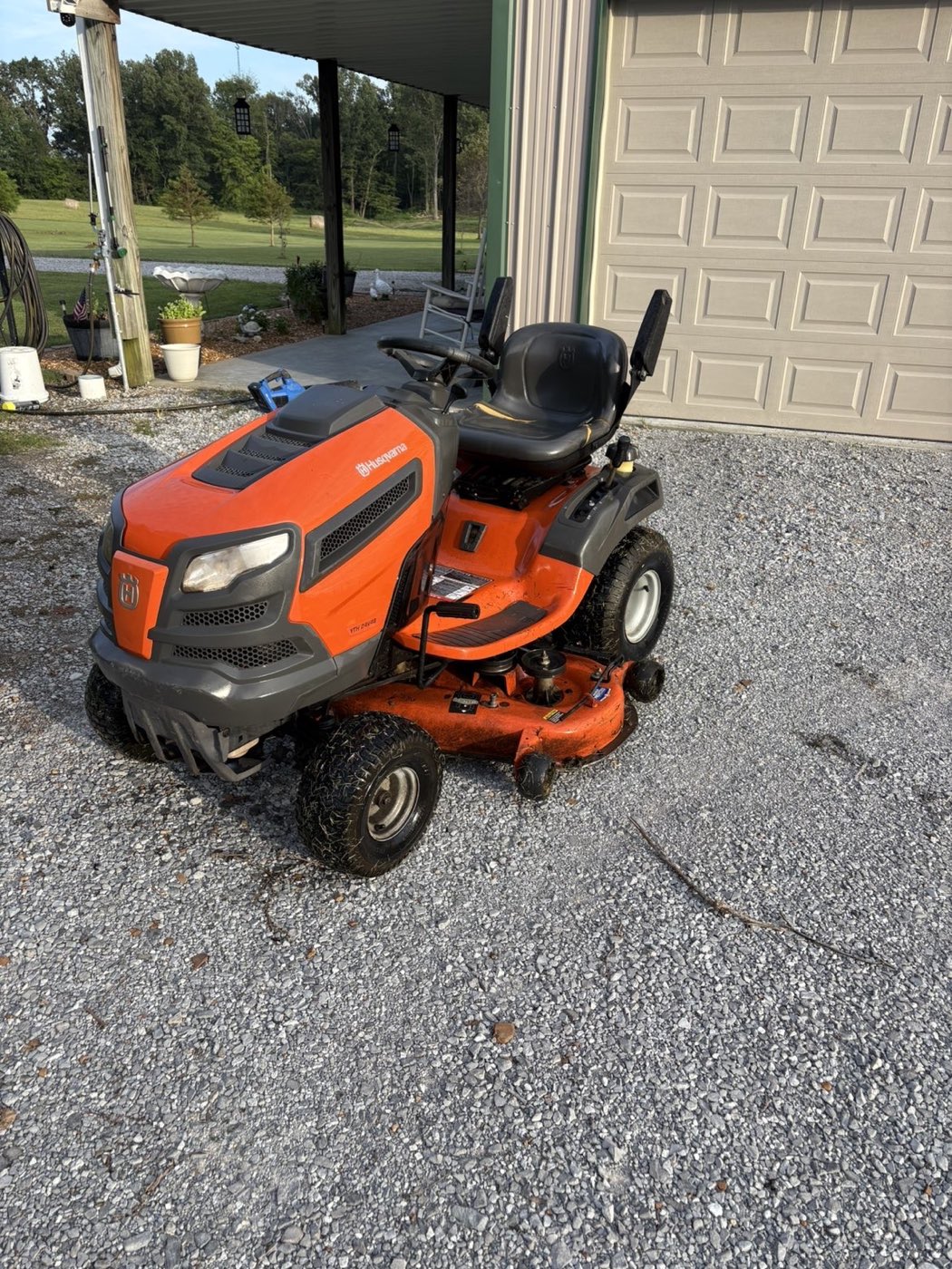 A Husqvarna YTH riding mower CJ repaired, sitting on gravel outside a barn